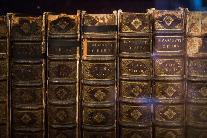 Livros antigos com as obras de Santo Agostinho, dispostos em close sobre uma superfície.