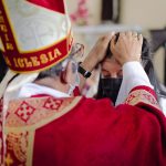 Bispo abençoa um participante durante uma celebração religiosa em uma igreja.
