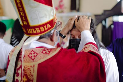 Bispo abençoa um participante durante uma celebração religiosa em uma igreja.