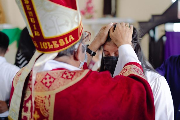 Bispo abençoa um participante durante uma celebração religiosa em uma igreja.