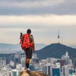 Homem com mochila observa a paisagem urbana de Seul do alto de uma montanha.