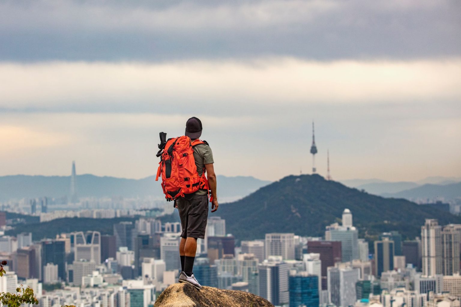 Homem com mochila observa a paisagem urbana de Seul do alto de uma montanha.