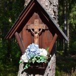 Crucifixo de madeira com flores preso a uma árvore em uma floresta tranquila