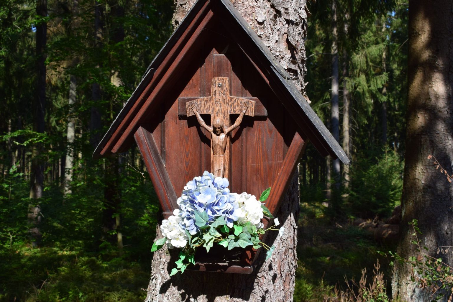 Crucifixo de madeira com flores preso a uma árvore em uma floresta tranquila