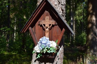 Crucifixo de madeira com flores preso a uma árvore em uma floresta tranquila