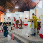 Crianças participam de uma celebração católica conduzida por sacerdotes dentro de uma igreja.