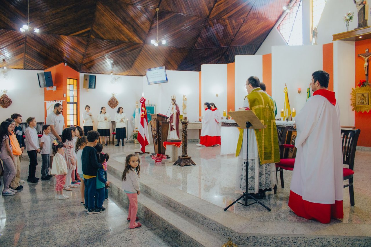 Crianças participam de uma celebração católica conduzida por sacerdotes dentro de uma igreja.