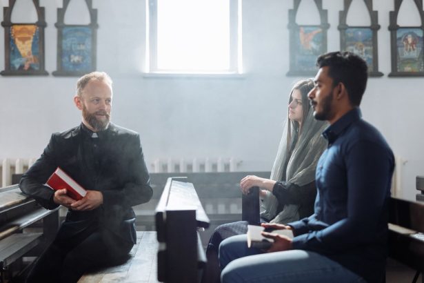 Padre conversa com duas pessoas no interior de uma igreja, em uma cena de diálogo e convivência comunitária.