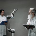 Dois pesquisadores em laboratório analisam um braço robótico durante um trabalho de desenvolvimento tecnológico.