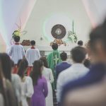 Fiéis participam de uma missa católica em uma igreja, acompanhados por um sacerdote diante do altar.