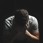 Homem em sofrimento emocional, com expressão triste e as mãos próximas ao rosto, em ambiente escuro