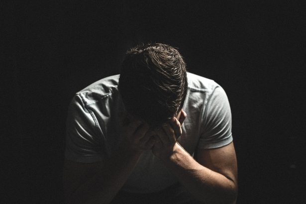Homem em sofrimento emocional, com expressão triste e as mãos próximas ao rosto, em ambiente escuro