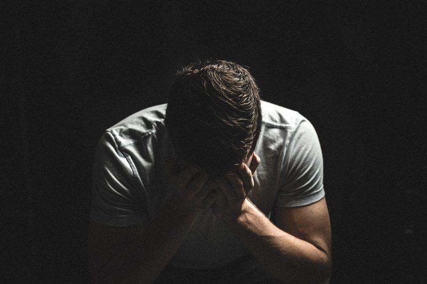 Homem em sofrimento emocional, com expressão triste e as mãos próximas ao rosto, em ambiente escuro